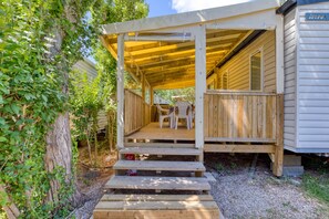 Eine Holzterrasse mit Stufen zu einem überdachten Veranda-Bereich, einem kleinen Tisch und zwei Stühlen.