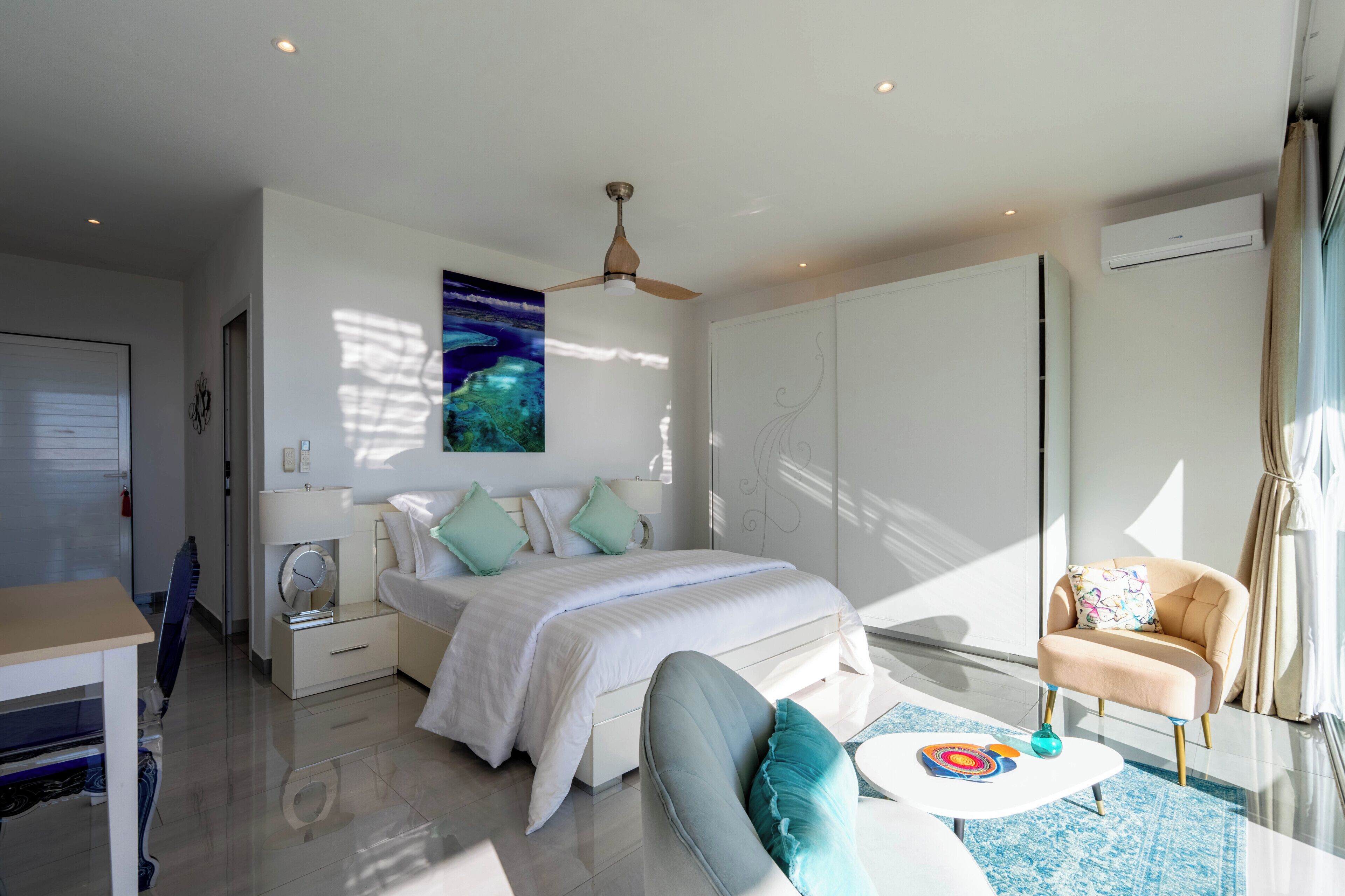 A modern bedroom with a bed, bedside tables, a chair, a ceiling fan, and a large window.
