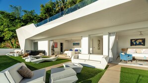 Un espacio exterior moderno con mobiliario blanco, una piscina y un porche cubierto.