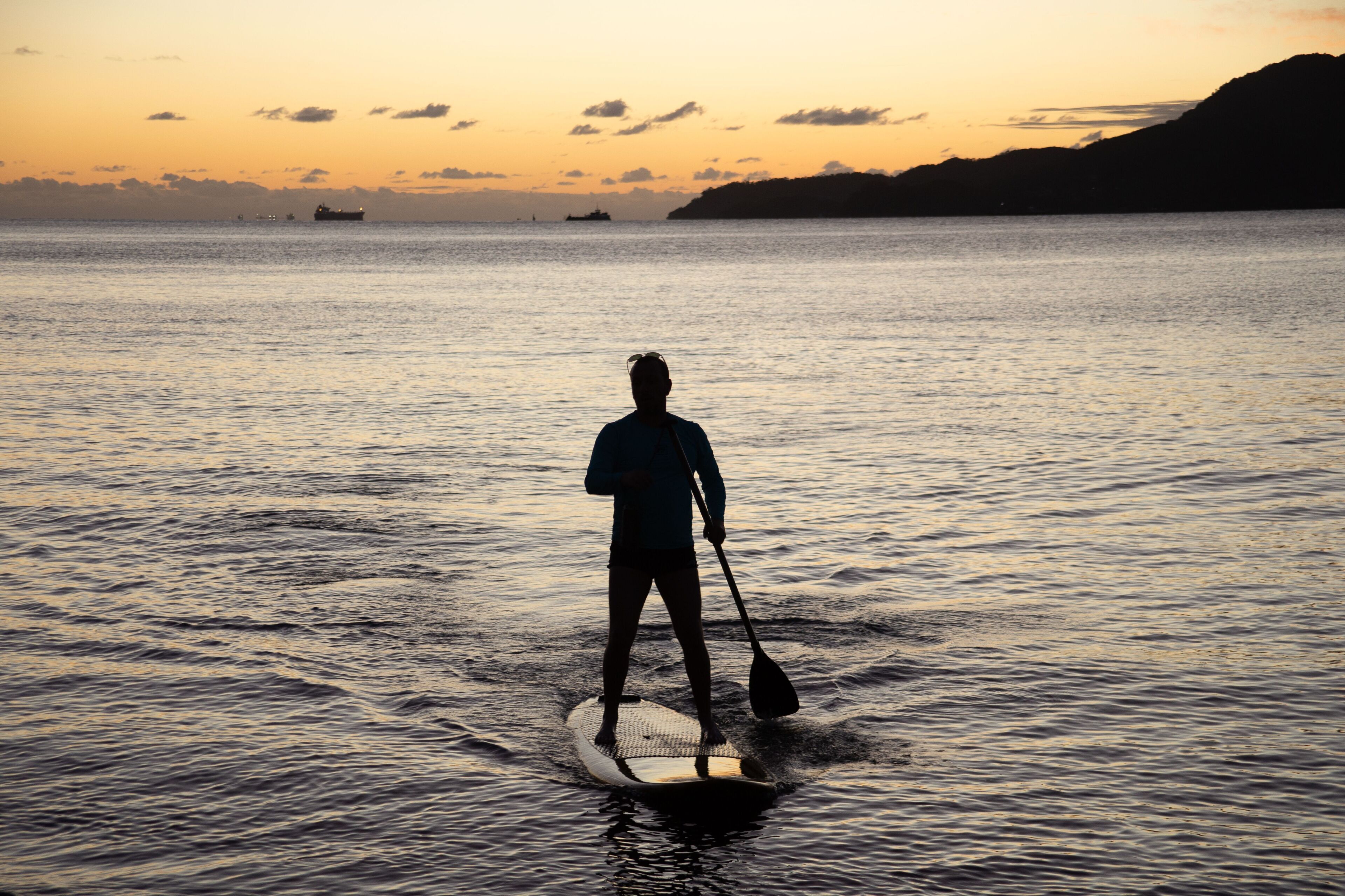 Una persona haciendo paddleboard en aguas tranquilas durante el atardecer.