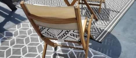 An outdoor patio with a round wooden table and two chairs, a patterned rug, and a white cushioned seating area.