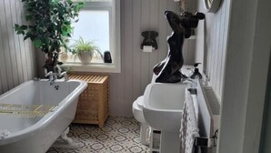 Un baño con una bañera independiente, un lavabo, un espejo y una planta en maceta.