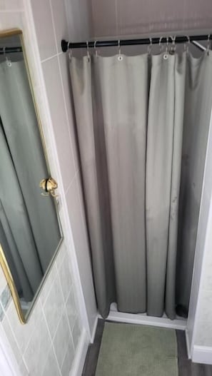 Un baño con cortina de ducha, una puerta con picaporte dorado y un tapete pequeño en el suelo.