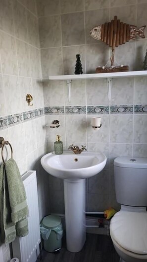 Baño con lavamanos pedestal, inodoro y repisa con objetos decorativos.