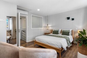 A bedroom with a bed, bedside tables, a hanging light fixture, and a potted plant.