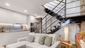 A modern living room with a sectional sofa, a wooden coffee table, and a staircase with a metal railing. - Casa ao Lado – In the Heart of Ponte de Lima with Private Entrance and Full Comfort (Ponte de Lima)