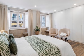 Habitació d'hotel amb un llit, dues cadires, una taula petita, una planta en testos i una finestra amb cortines.