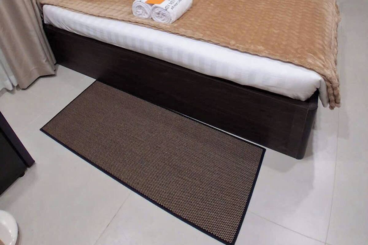 Una cama bien tendida con una manta marrón y sábanas blancas, una toalla enrollada y una pequeña alfombra.