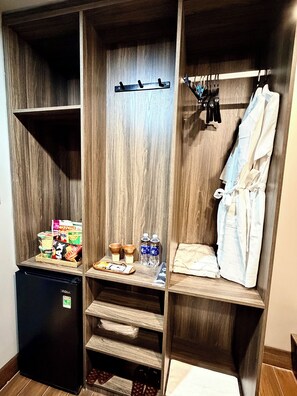 A walk-in closet with wooden shelving, a hanging robe, and a small refrigerator.