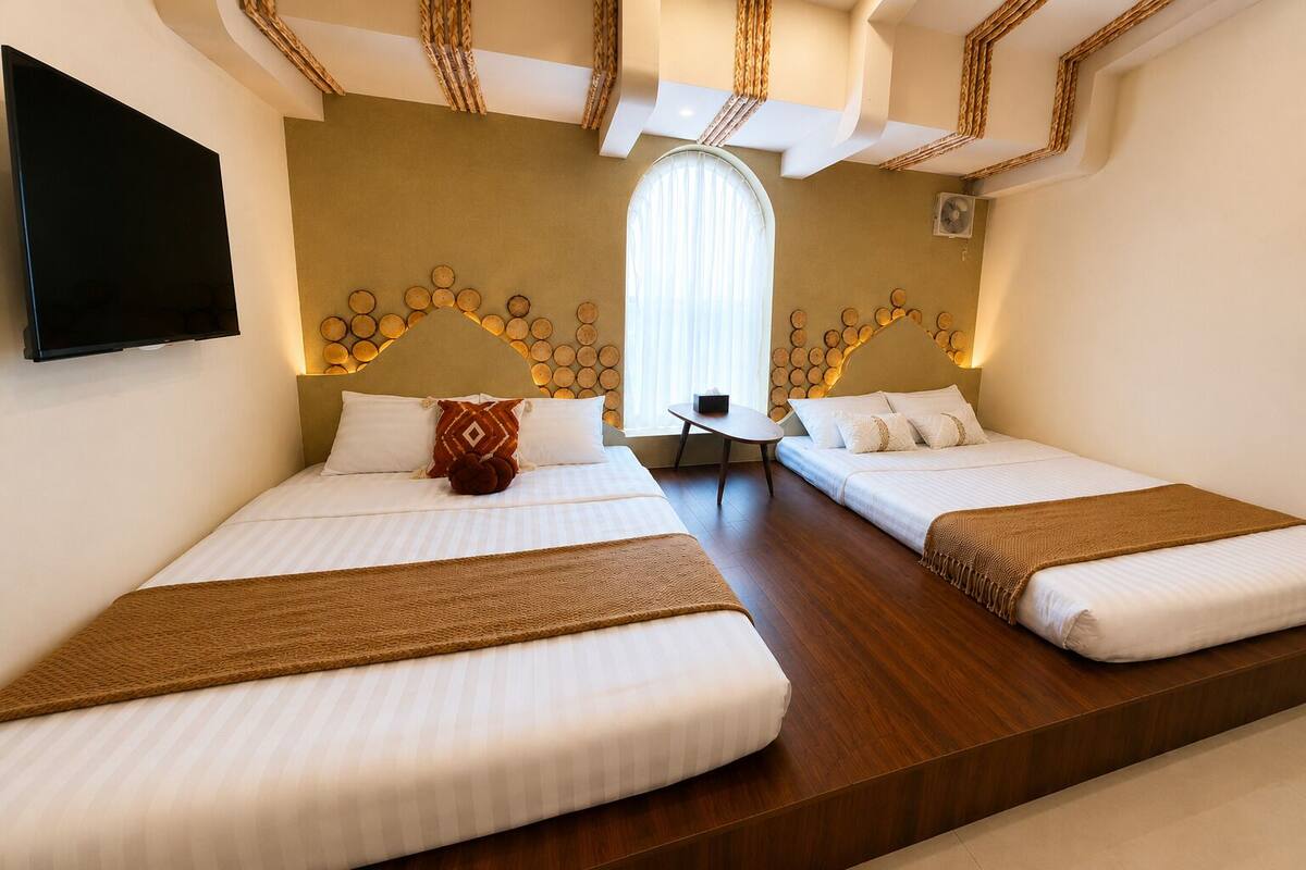 Habitación de hotel con dos camas, una mesita, televisor y un ventanal grande.