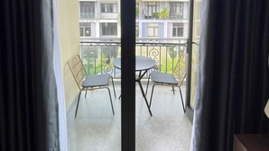 A balcony with a table and chairs, a view of the neighborhood, and a door with curtains.