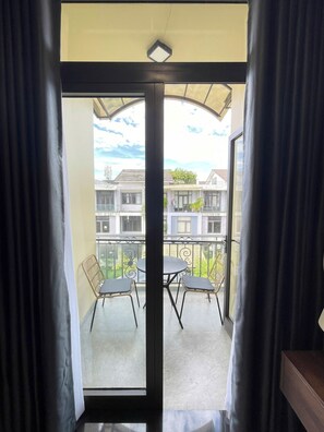 A balcony with a table and chairs, a view of the neighborhood, and a door with curtains.
