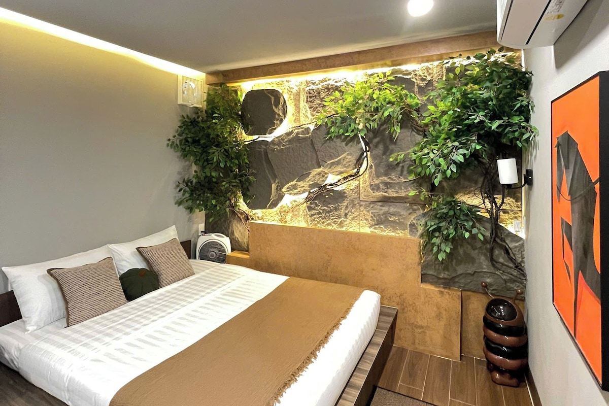 A modern bedroom with a bed, a wall-mounted air conditioner, and a decorative rock wall with plants.