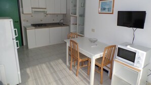 Een compacte keuken met witte kastjes, een eettafel met stoelen, een magnetron en een televisie aan de muur.