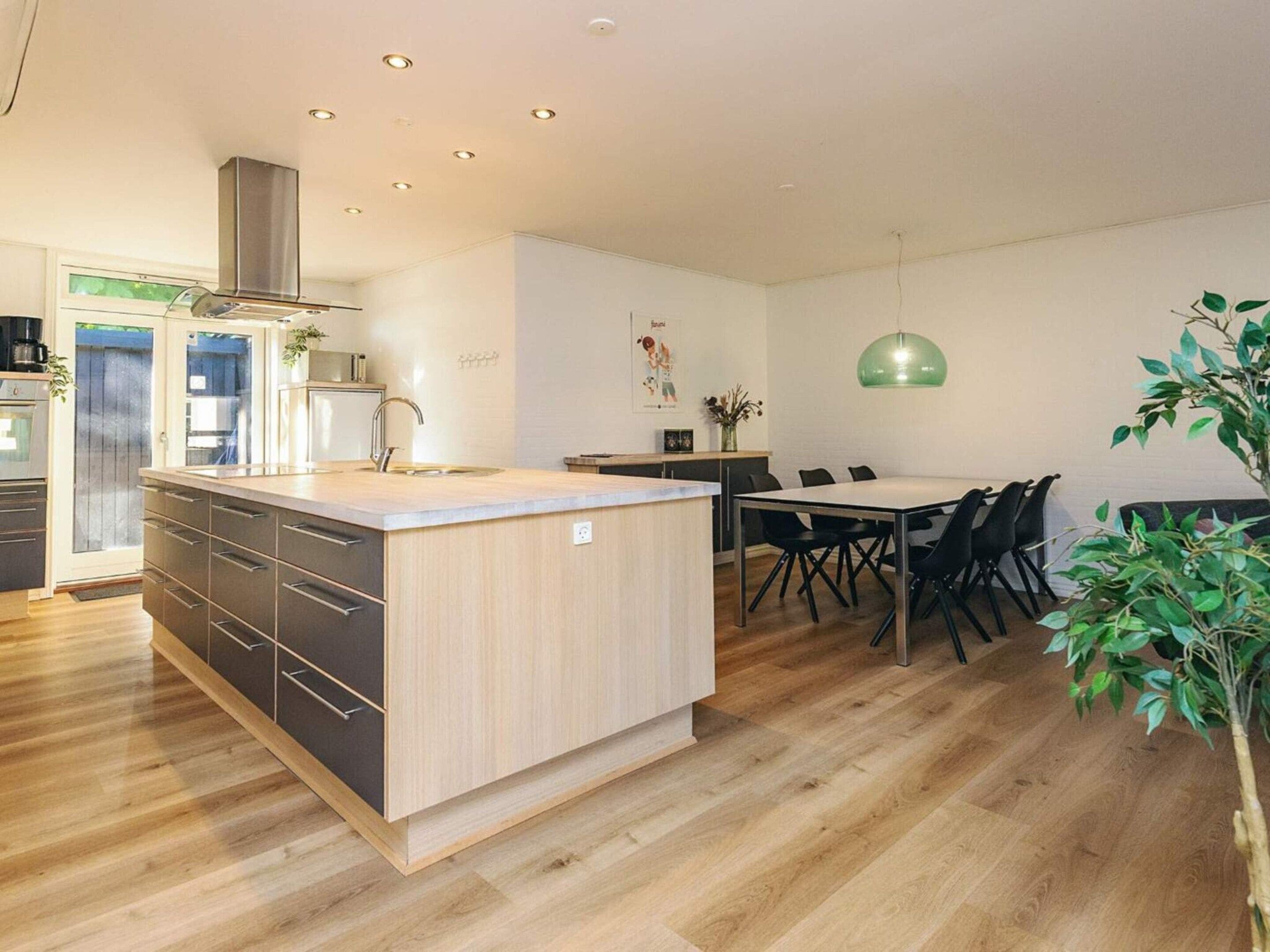 Una cocina moderna con una isla central, suelo de madera y un comedor con mesa y sillas.