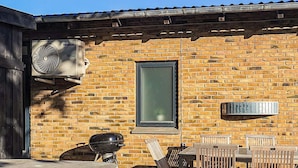 An outdoor patio with a brick wall, a table, chairs, a grill, and a window. - 4 Star Holiday Home in Skagen (Skagen)