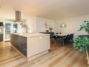 Cozinha moderna com ilha central, piso de madeira e área de jantar com mesa e cadeiras.