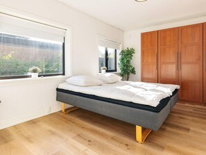 Quarto com cama, guarda-roupa de madeira, janelas e um vaso de planta.