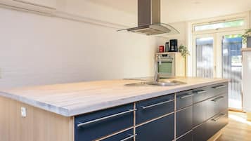 Una cocina moderna con horno empotrado, un lavamanos de acero inoxidable y una campana de cristal.