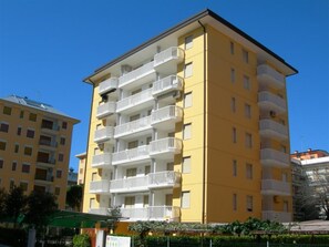 Ein mehrstöckiges, gelbes Gebäude mit Balkonen, einer grünen Markise und blauem Himmel.