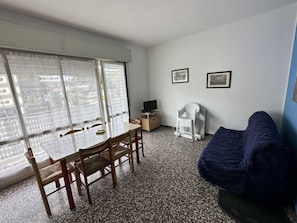 Ein Zimmer mit Esstisch, Stühlen, Fernseher, Sofa und zwei gerahmten Bildern an der Wand.