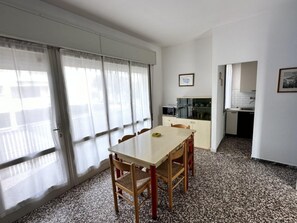 Ein Zimmer mit Esstisch, Stühlen, einer Küchenzeile und einem fenster mit Vorhängen.