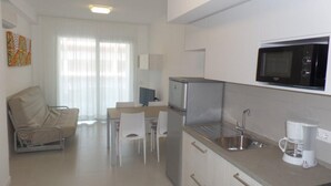 A compact kitchen with a microwave, coffee maker, and a refrigerator. There is a dining area with a table and chairs. - Sunny accommodation with rooftop pool (Bibione)