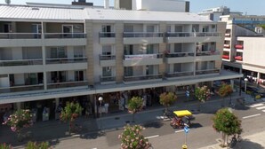 A multi-story hotel with balconies, a ground floor with shops, and a street view with pedestrians and vehicles. - Sunny accommodation with rooftop pool (Bibione)