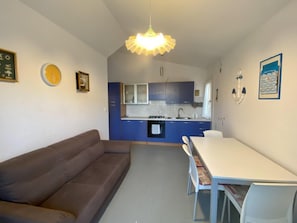 Eine moderne Küche mit blauen Schränken, einem Esstisch mit Stühlen, einer Couch und einer Pendelleuchte.