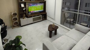 A living room with a TV, sofa, and a balcony with a view. - Your Home in Barranquilla (Barranquilla)