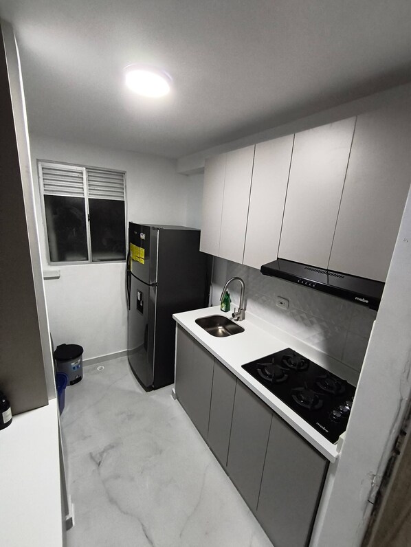 Una cocina compacta con refrigerador, estufa, lavamanos y armarios.