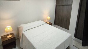A bedroom with a bed, two bedside lamps, an air conditioning unit, and a wardrobe. - Your Home in Barranquilla (Barranquilla)