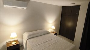 A bedroom with a bed, two bedside lamps, an air conditioning unit, and a wardrobe. - Your Home in Barranquilla (Barranquilla)