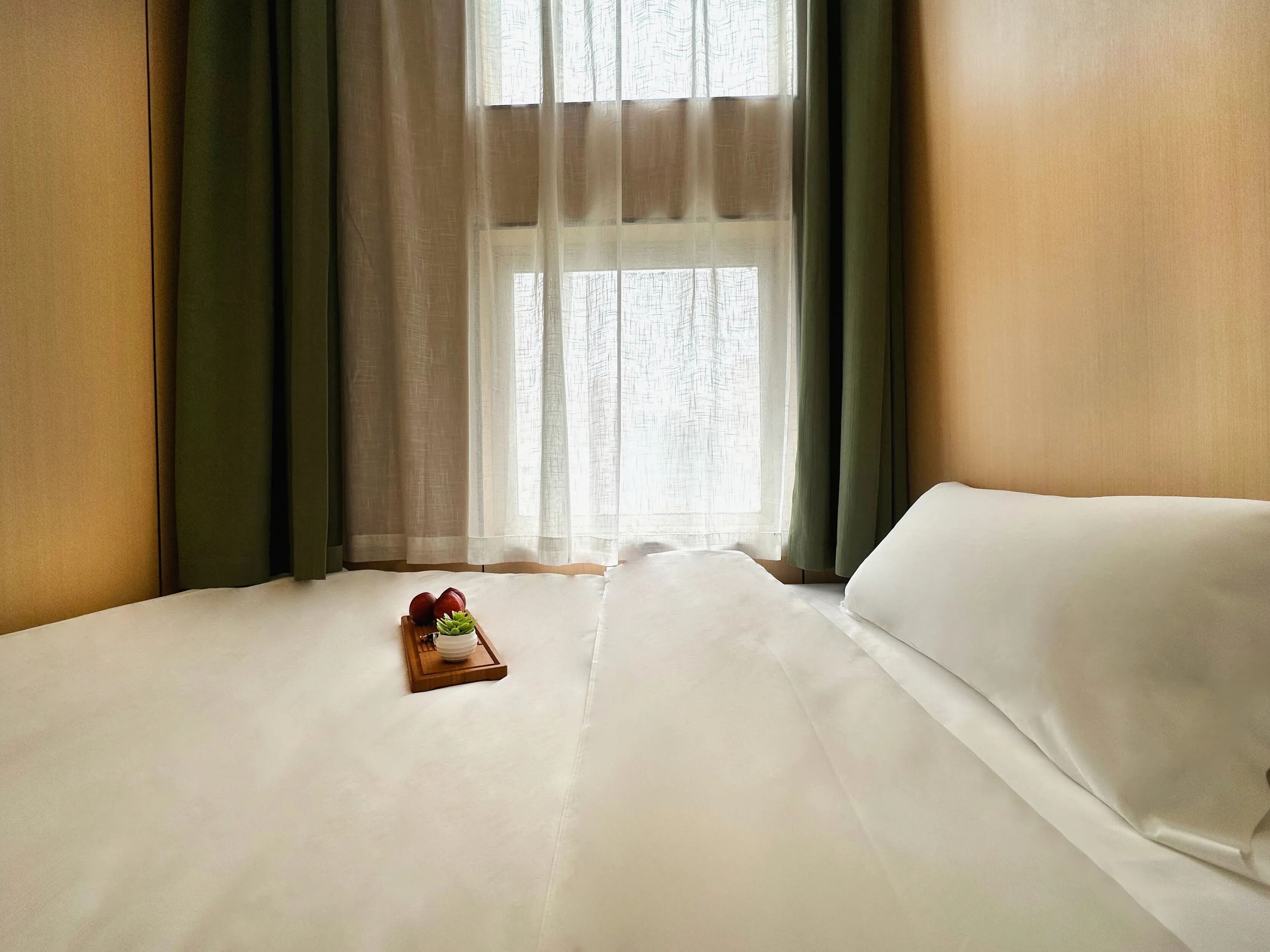 Een hotelkamer met een bed, een klein houten dienblad met fruit en dunne gordijnen.