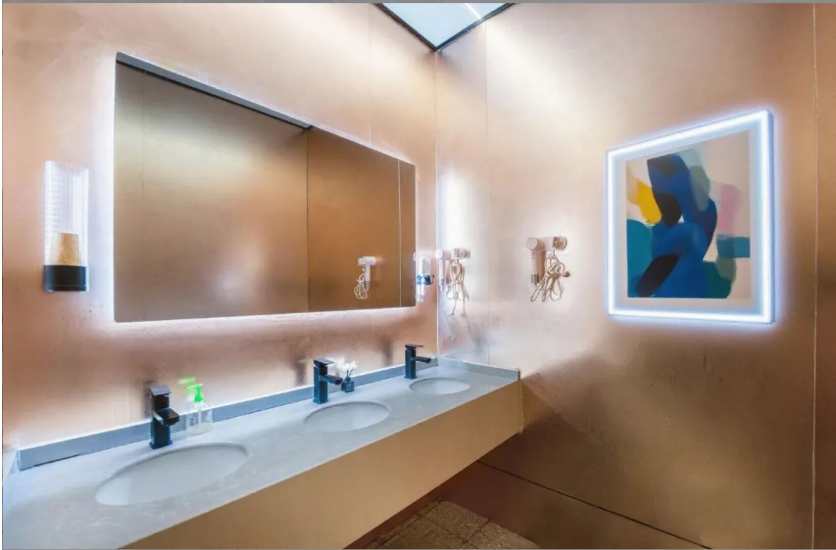 A modern bathroom with a large mirror, three sinks, and a wall-mounted art piece.