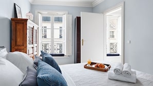 A bedroom with a bed, pillows, a tray with breakfast, and a view of buildings through the window. - Chic 1BR Near Opéra & Louvre (Paris)