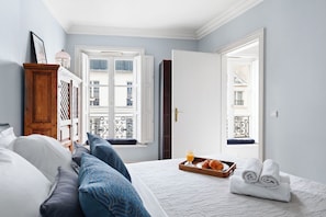 Ein Schlafzimmer mit Bett, Kissen, einem Tablett mit Frühstück und Blick auf Gebäude durch das Fenster.