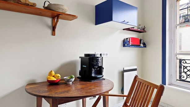 A kitchen with a coffee maker, a bowl of fruit, and a chair. - Chic 1BR Near Opéra & Louvre (Paris)
