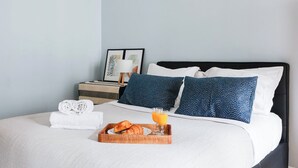 A neatly made bed with pillows, a tray with croissants and orange juice, and a bedside table with a lamp and framed artwork. - Chic 1BR Near Opéra & Louvre (Paris)