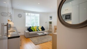 Une cuisine moderne équipée d’un four à micro-ondes encastré, un canapé gris agrémenté de coussins colorés, une petite table basse et un grand miroir mural.