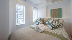 Une chambre à coucher avec un lit, des oreillers, une fenêtre et une œuvre d’art murale.