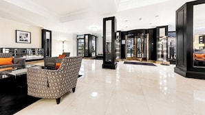 Un hall d’entrée spacieux au design moderne, comprenant un coin salon avec des canapés à motifs et une table basse, un grand miroir et un ascenseur en verre.