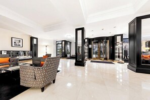 Eine geräumige Lobby mit modernem Design, ausgestattet mit einer Sitzecke mit gemusterten Sofas und einem Couchtisch, einem großen Spiegel und einem gläsernen Aufzug.