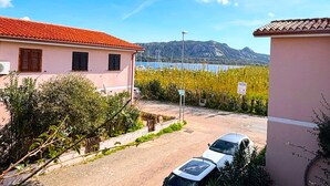 Ein Wohngebiet mit einer Reihe geparkter Autos, einem Gebäude mit rotem Ziegeldach und freiem Blick auf Meer und Berge im Hintergrund.