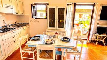 Uma sala de jantar com mesa posta para quatro pessoas, armários de cozinha, fogão e janela com cortinas.