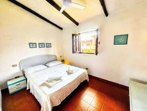 Een slaapkamer met een bed, nachtkastje, raam met uitzicht en plafondventilator.