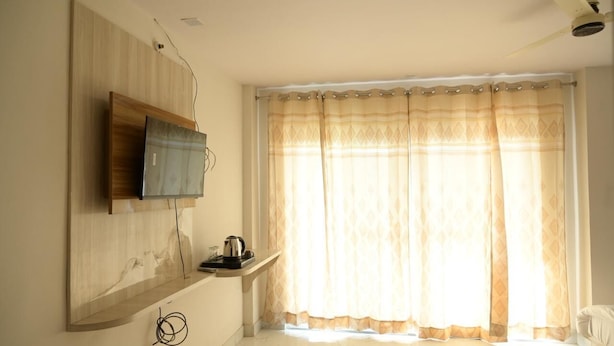 A room with a mounted television, a coffee maker on a shelf, and a large window with patterned curtains. - Hotel Deep Khirsu (Khirsu)