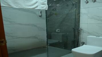 A bathroom with a glass shower enclosure, a toilet, and a marble-tiled wall.