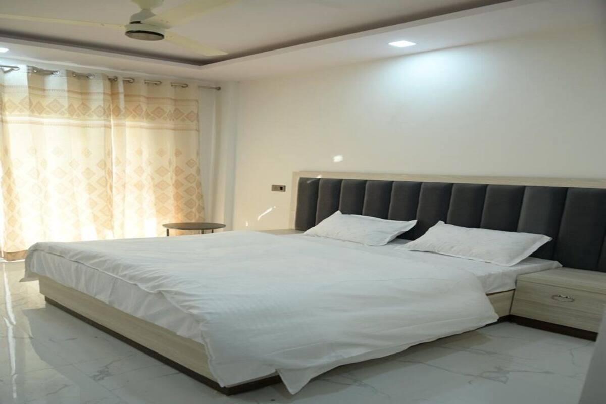 A bedroom with a large bed, a bedside table, a nightstand, a ceiling fan, and a window with curtains.