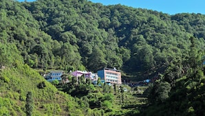 A hillside with terraced fields and buildings with multiple floors and balconies. - Hotel Deep Khirsu (Khirsu)
